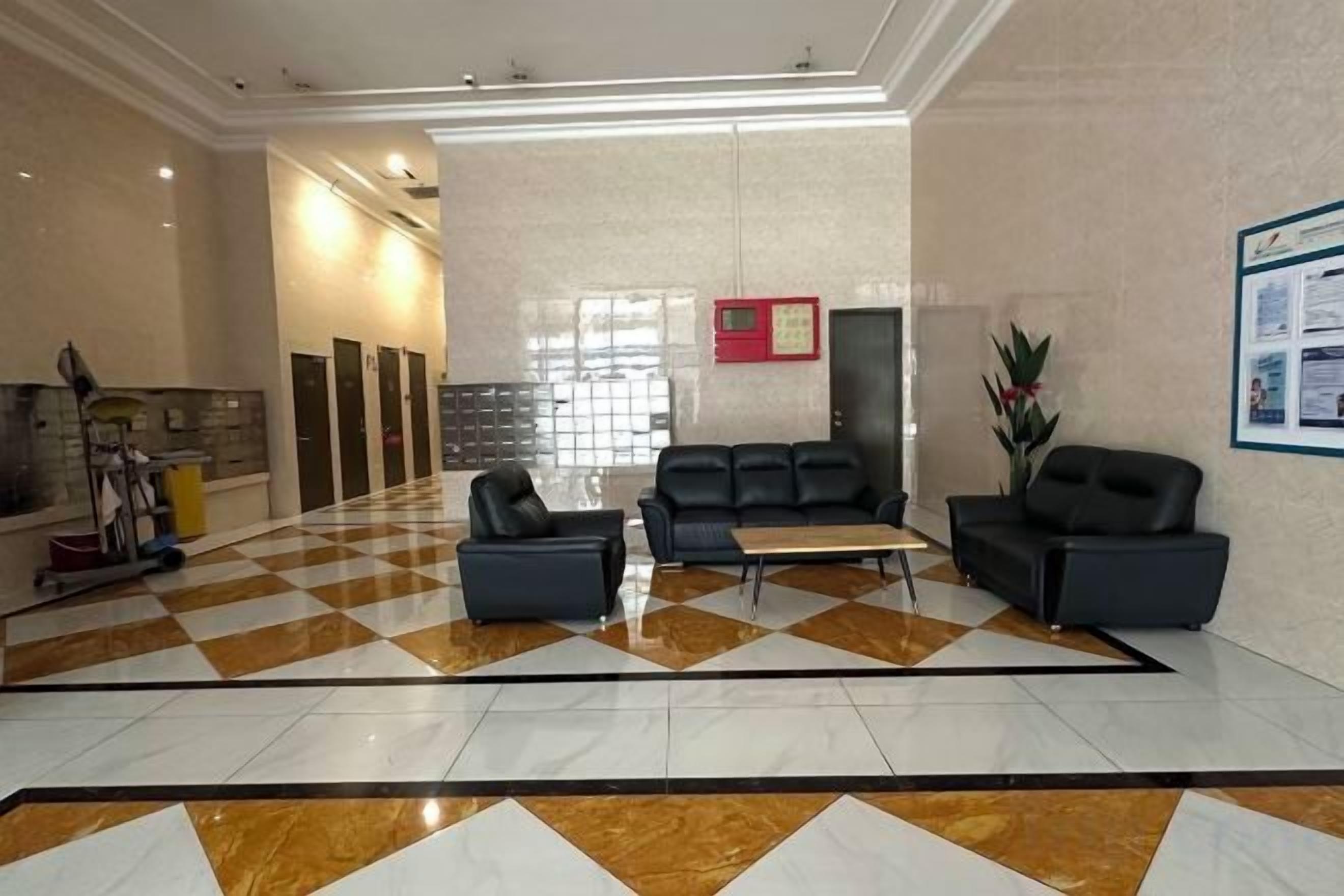A hotel lobby with a checkered floor, a reception desk, seating area, and a wall-mounted information board.