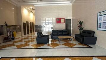 A hotel lobby with a checkered floor, a reception desk, seating area, and a wall-mounted information board.