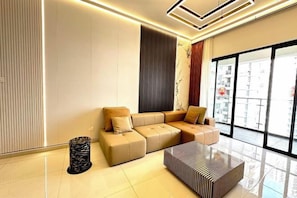 A modern living room with a sectional sofa, a coffee table, and a large window offering a view of the city.