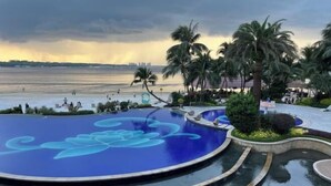 Una gran piscina circular con diseño azul, rodeada de palmeras y vista a la playa.