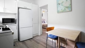 A compact kitchen with white cabinetry, a microwave, and a refrigerator. There is a dining area with a wooden table and two chairs. - Sammy's Seaside Hideaway in Henley Beach (Henley Beach South)