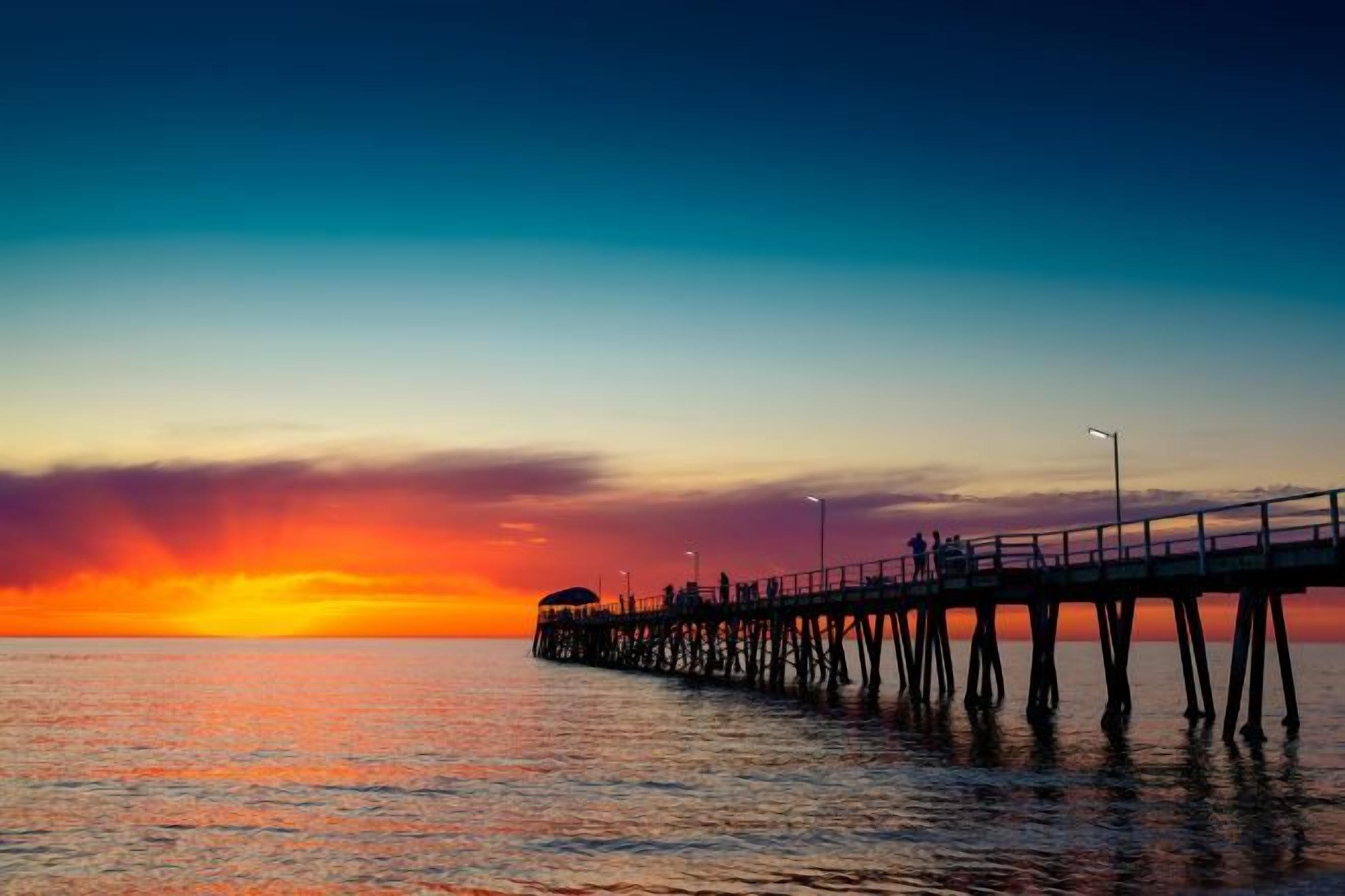 A pier extending into calm waters with a sunset in the background.