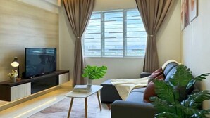 A modern living room with a flat-screen TV, a small table with a plant, a sofa, and a window with curtains. - D'Kayangan, Setia Ecohill Semenyih Serenity Suite (Semenyih)