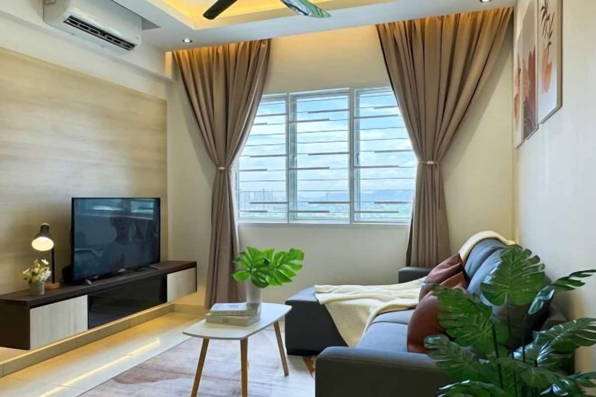 A modern living room with a flat-screen TV, a small table with a plant, a sofa, and a window with curtains.