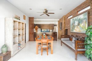 A dining area with a wooden table and chairs, a ceiling fan, and a brick wall with a painting. - Umah Bali Villa (Bali)