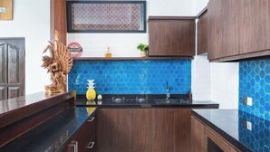 A kitchen with dark wooden cabinets, a black countertop, and a blue hexagonal tile backsplash. - Umah Bali Villa (Bali)
