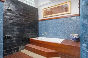 A bathroom with a stone wall, a bathtub, and a framed artwork. - Umah Bali Villa (Bali)