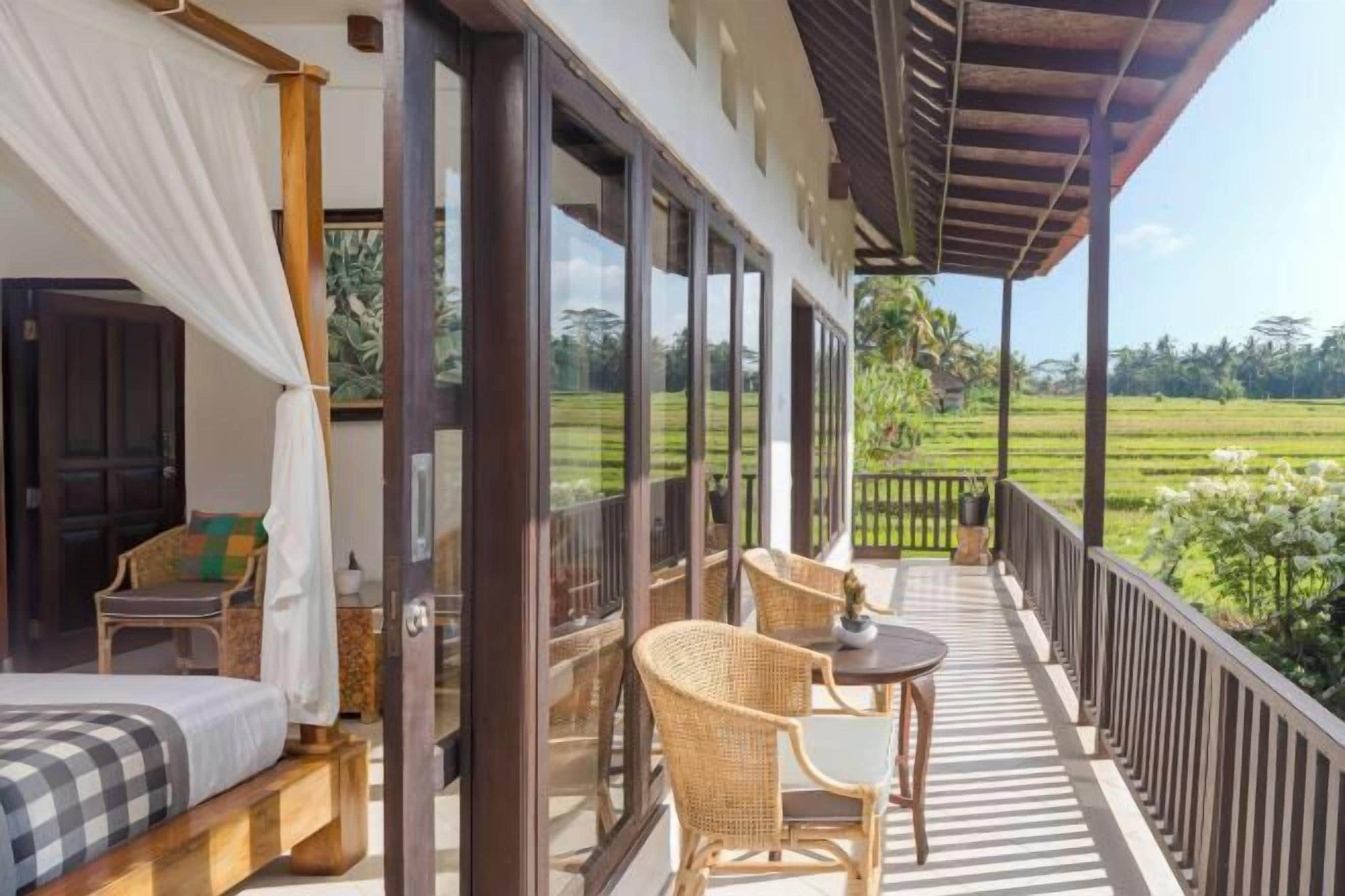 Un dormitorio con cama, una silla y una mesa en un balcón con vistas a un campo verde.