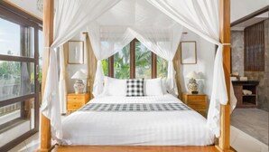 A four-poster bed with white bedding, wooden headboard, and canopy, flanked by nightstands with lamps, in a room with large windows and a view of greenery. - Umah Bali Villa (Bali)