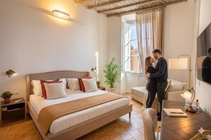 A hotel room with a large bed, bedside tables, a desk, a chair, a plant, and a window with curtains. - Amelie Suite Navona (Rome)