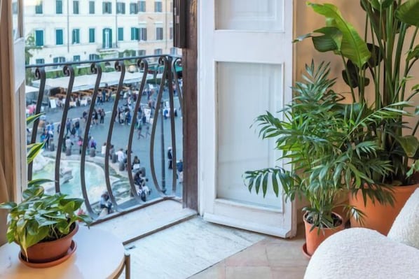 A balcony with a view of a busy street, potted plants, and a white chair.
