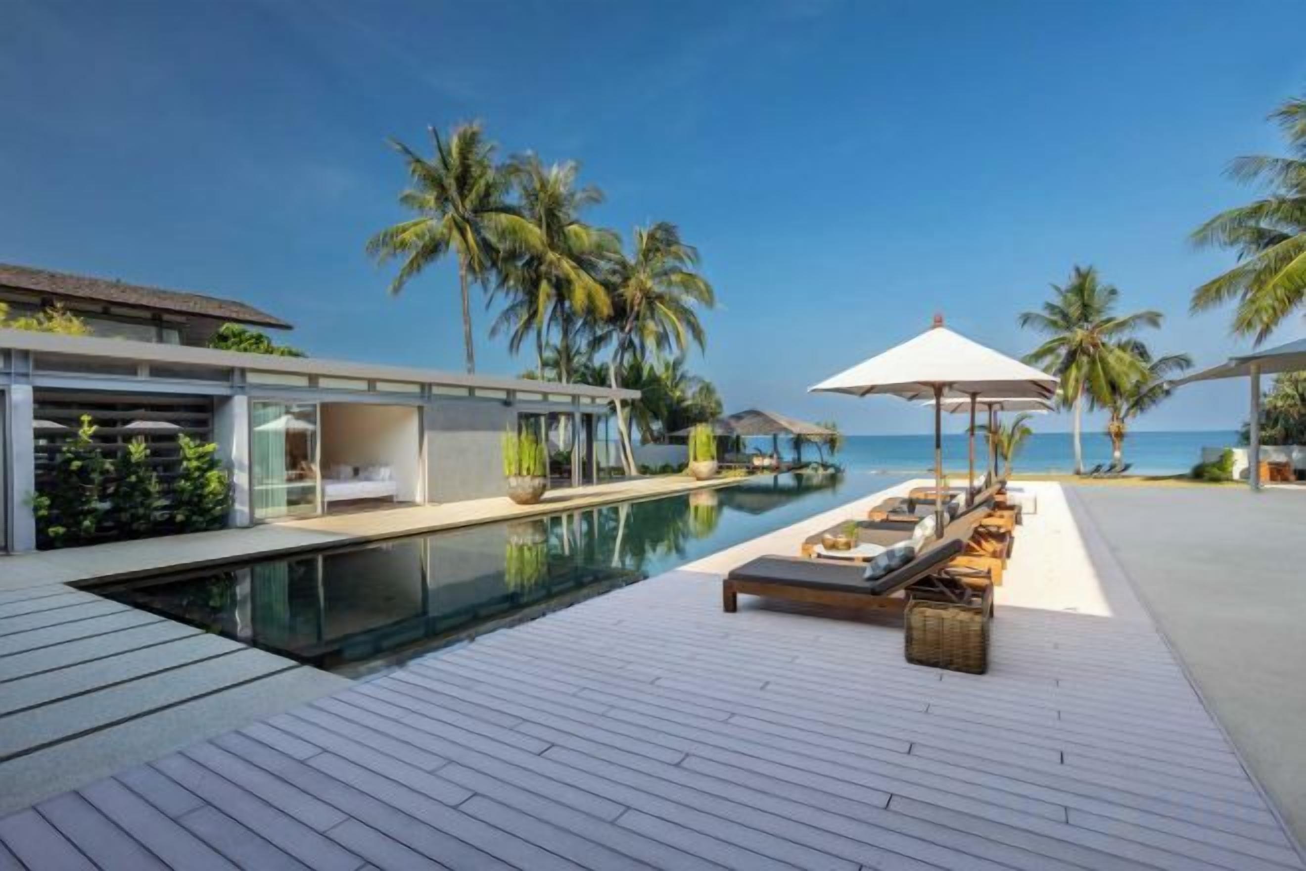 A modern resort with a pool, lounge chairs, and palm trees.