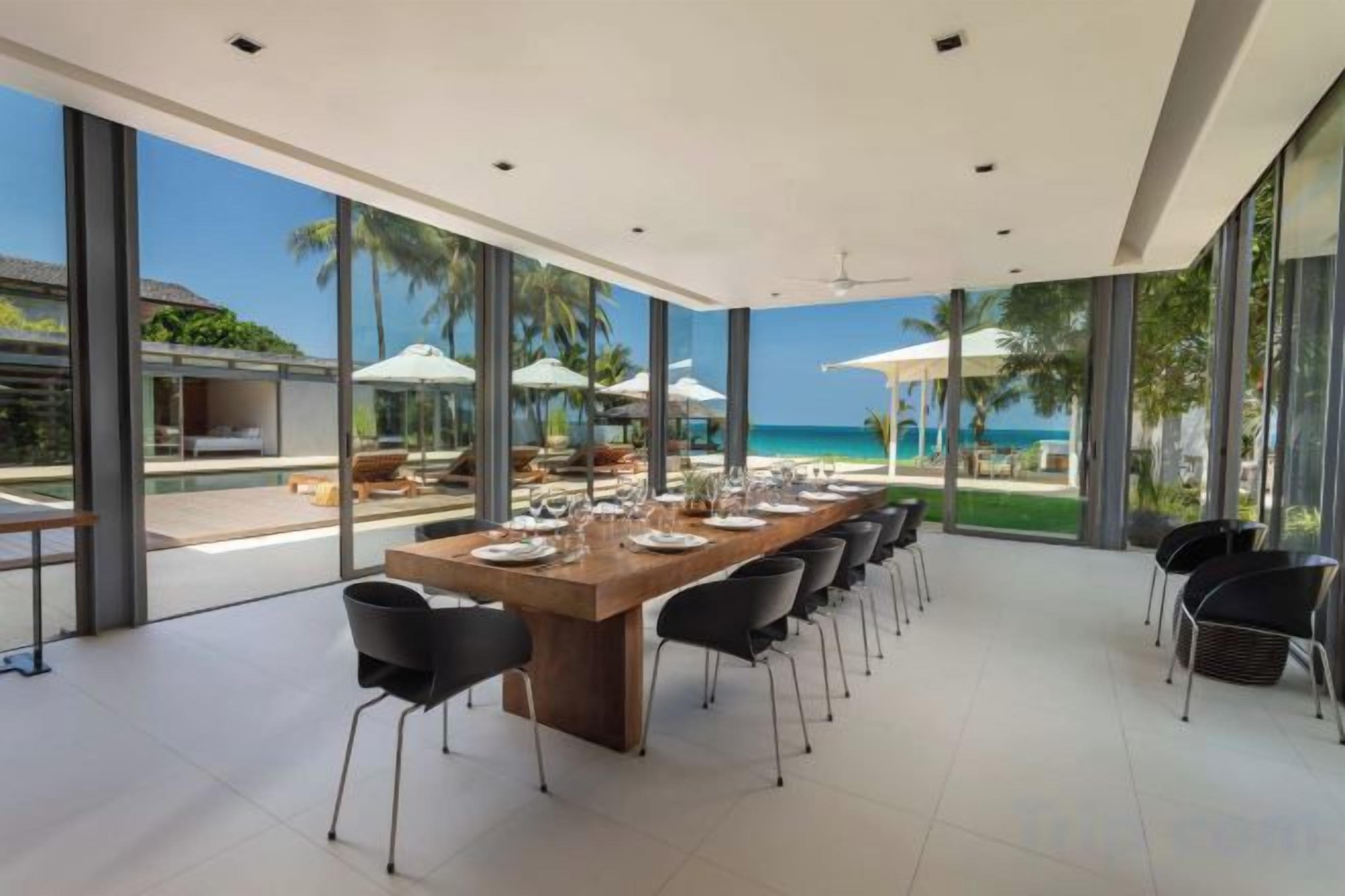 Un comedor amplio con una mesa larga y sillas, ventanas grandes y vistas a la playa.