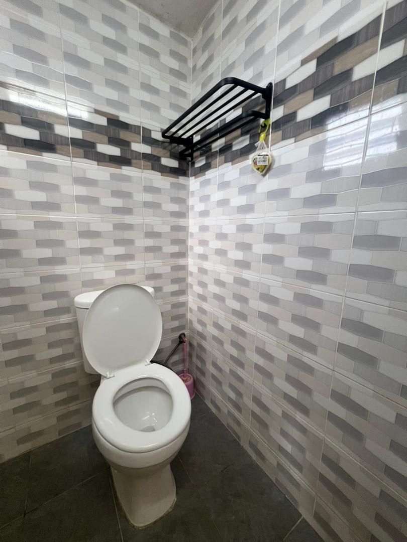 A small bathroom with a toilet, a black shelf with a yellow object, and a pink cleaning tool.