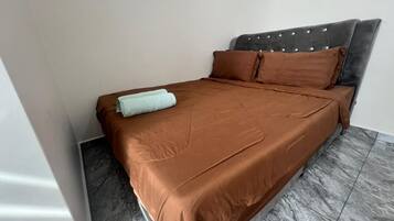 A bed with a brown bedspread and pillows, a grey upholstered headboard, and a grey tiled floor.