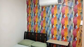A bedroom with a bed, a pillow, an air conditioning unit, and a colorful feather-patterned wall.