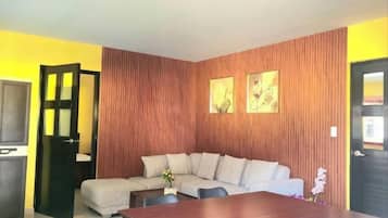 A living room with a sectional sofa, a dining table, and a TV.