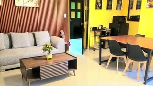 Ein Wohnzimmer mit einer Couch, einem Couchtisch und einem Esstisch mit Stühlen. Eine Tür führt in einen anderen Raum.