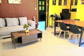 A living room with a sofa, coffee table, and dining table with chairs. There is a door leading to another room. - Jenessa's Executive-Suite near Lanuza Surf Bay (Madrid)