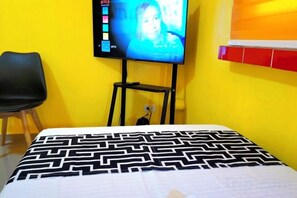 Een kamer met een bed, een aan de muur bevestigde televisie en een stoel.