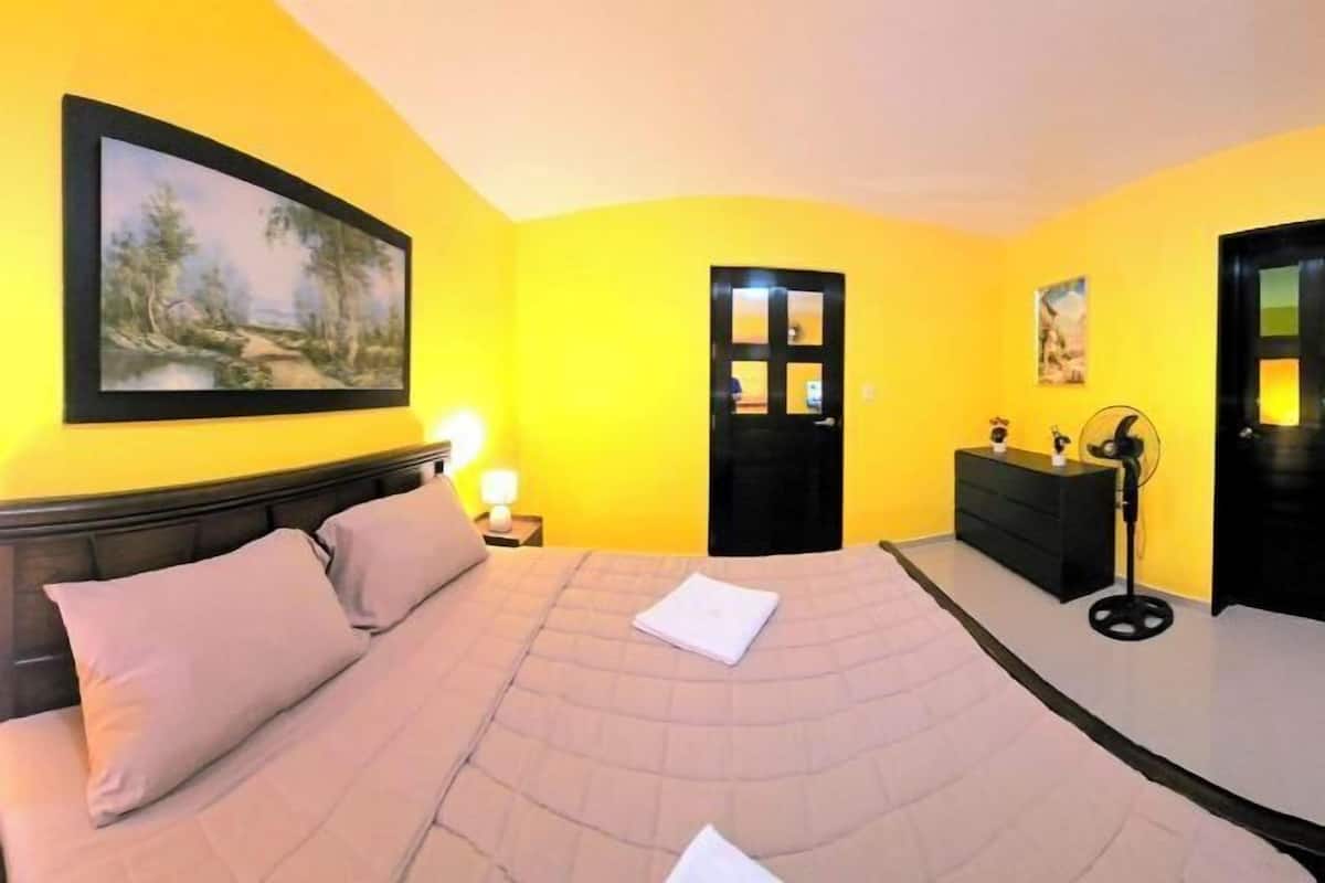 Une chambre à coucher avec un lit, une table de chevet, une commode, une porte et un tableau au mur.