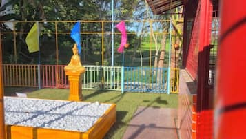 A fenced outdoor area with a play structure, a small garden bed, and a pathway.