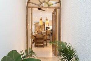 Un acceso a un comedor con una mesa y sillas, un ventilador de techo y lámparas colgantes.