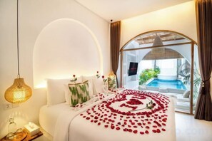 Habitación de hotel con cama, mesita de noche, lámpara y vista a una piscina.