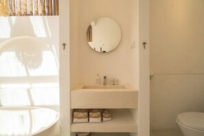 Un baño con un espejo redondo, un lavabo y un inodoro.
