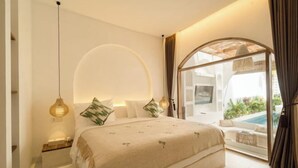 A bedroom with a bed, bedside tables, a hanging light fixture, and a view of an outdoor pool area. - Brand New Villa 2Br with Private Pool Near Seminyak by BaliSuperHost (Bali)