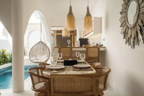 Un comedor con mobiliario de mimbre, vista a la piscina y lámparas colgantes.