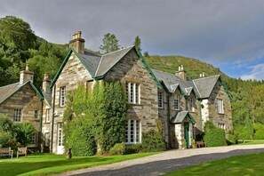 A stone building with multiple chimneys, a well-maintained lawn, and a hill in the background. - Chesthill House & Estate, Glenlyon (Aberfeldy)