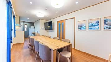 A dining area with a wooden table and chairs, a TV mounted on the wall, and framed pictures on the wall.