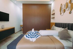 A hotel room with a bed, a flat-screen TV mounted on the wall, a wooden panel divider, and a decorative wall piece. - The Lavana Nakula Villa Kuta Sunset (Bali)