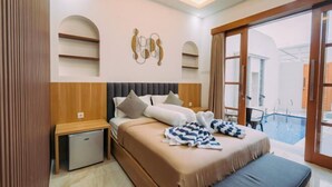 A modern hotel room with a large bed, a small desk, a refrigerator, and a view of an outdoor swimming pool. - The Lavana Nakula Villa Kuta Sunset (Bali)
