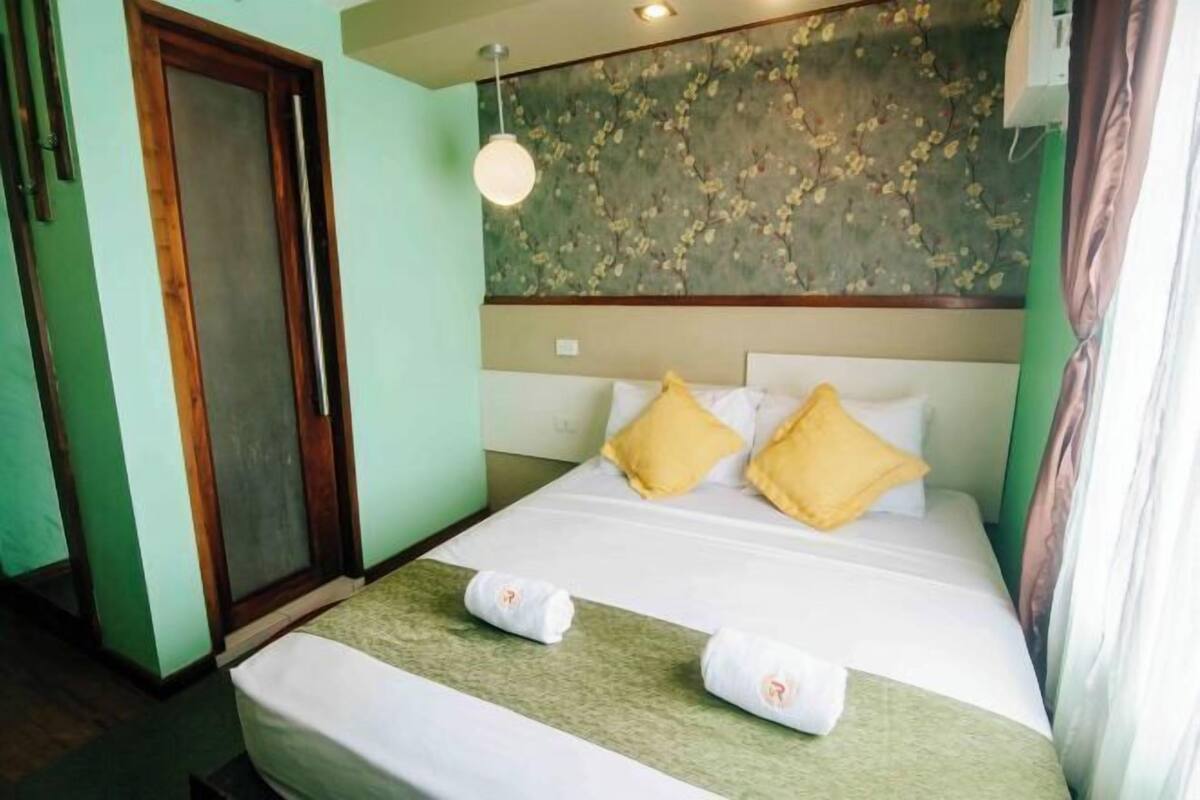 A hotel room with a bed, a green wall, a wooden door, and a ceiling light.
