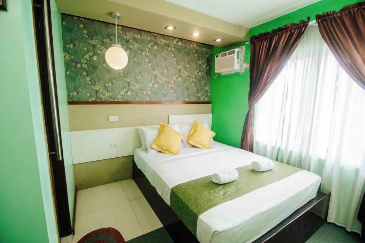 A hotel room with a bed, a wall-mounted air conditioner, and a window with curtains.