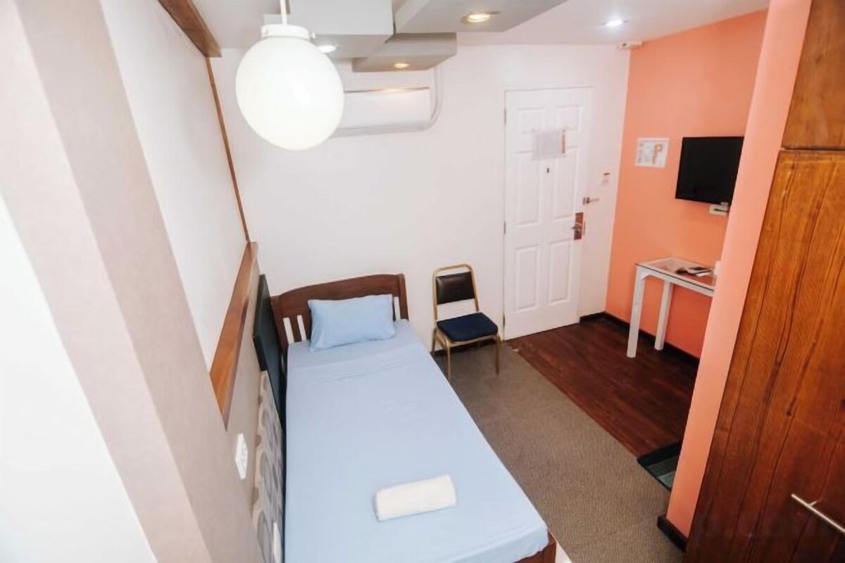 A compact room with a bed, a small table, a chair, and a television on the wall.