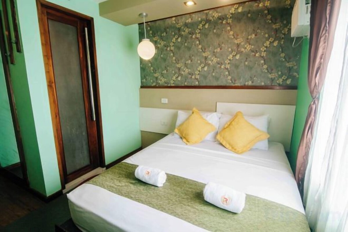 A hotel room with a bed, a door, and a wall with a floral pattern.