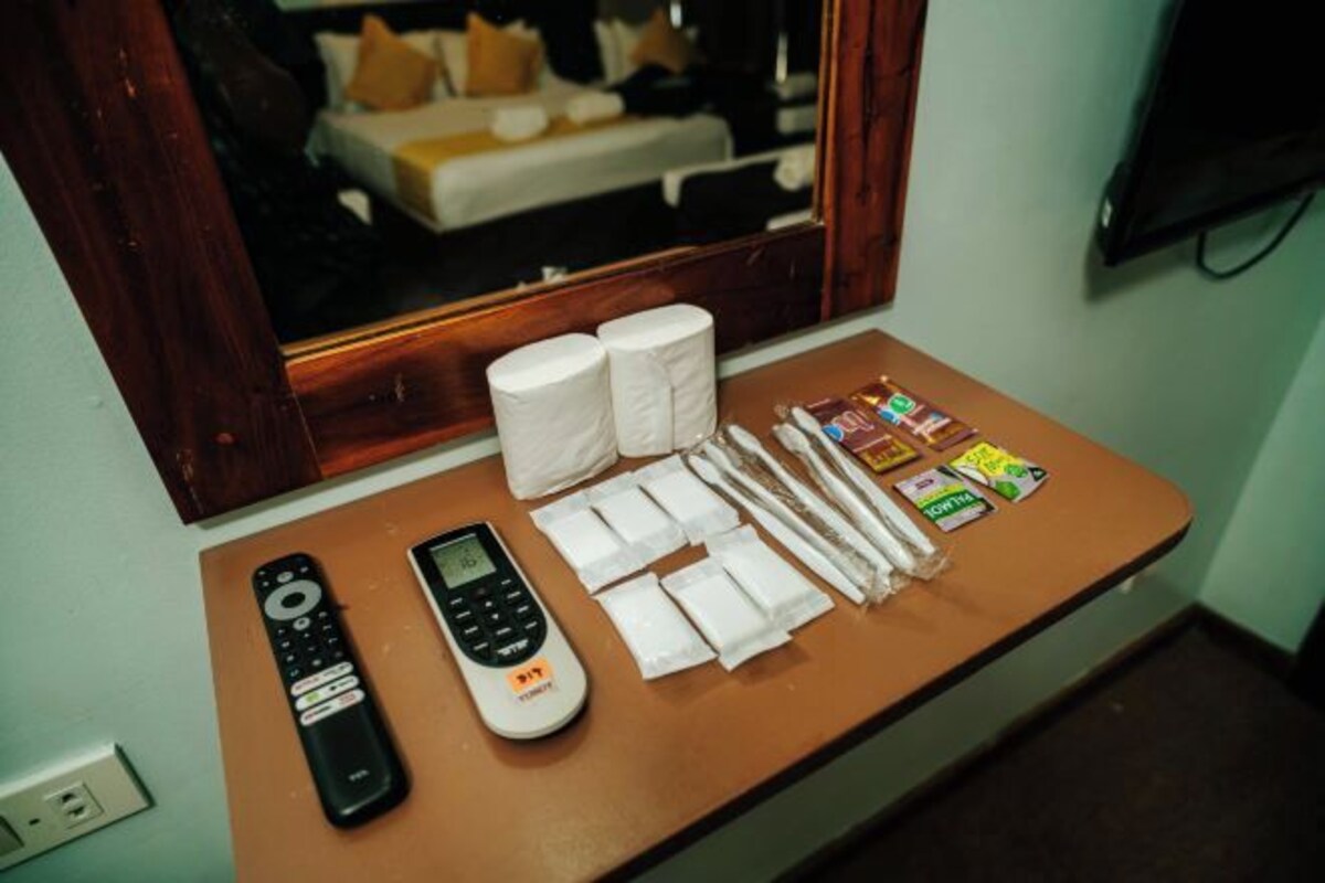 Quarto de hotel com cama, espelho, mesa de cabeceira com controle remoto, telefone, lenços de papel e artigos de higiene pessoal.