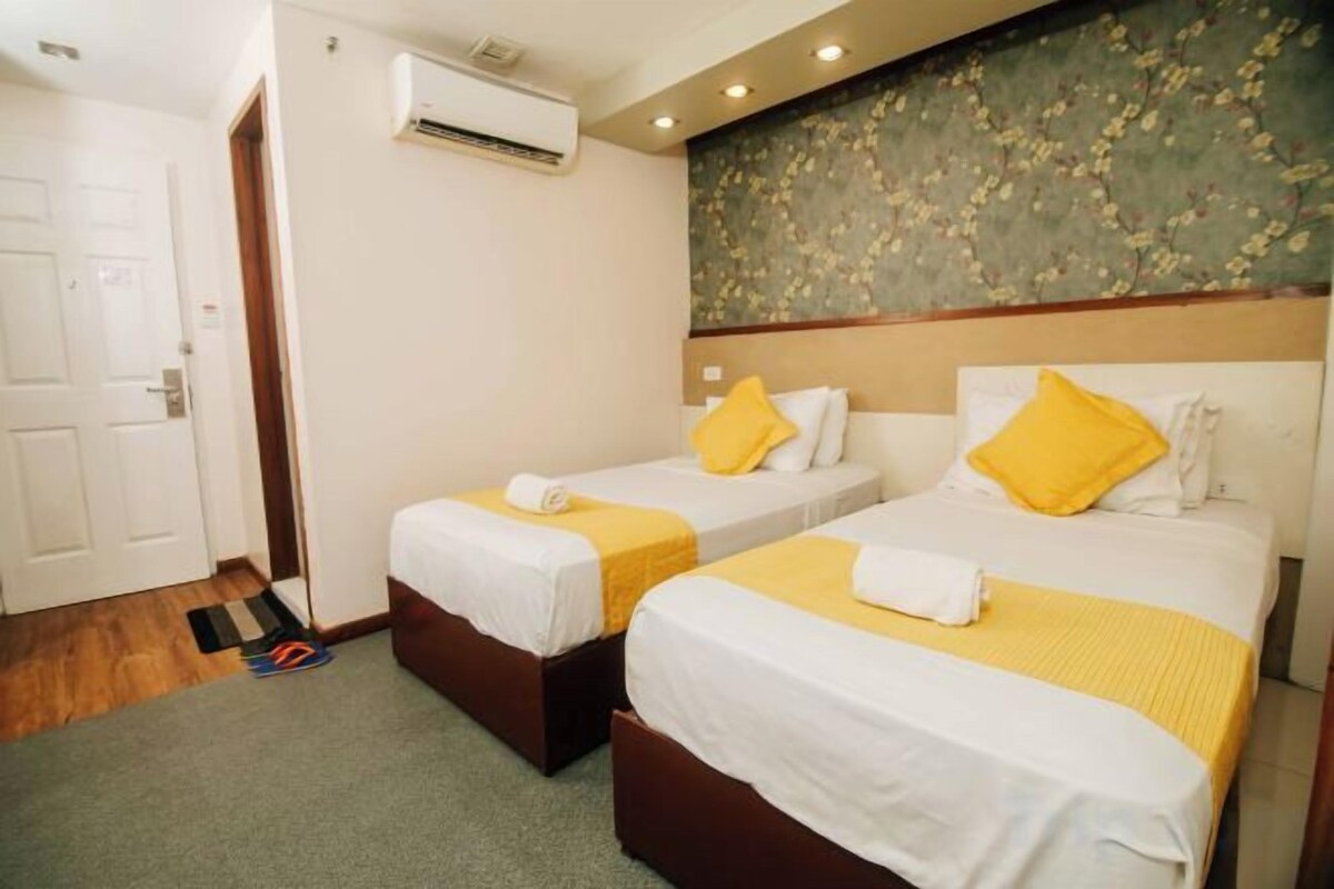 A hotel room with two beds, a door, and an air conditioning unit.
