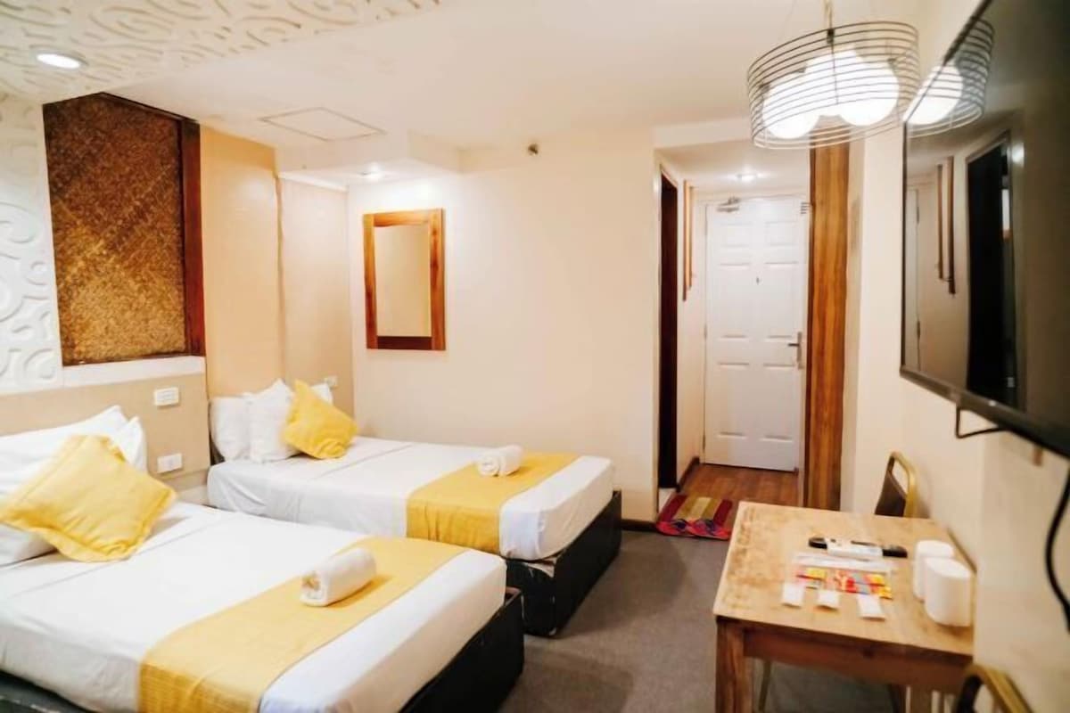 A hotel room with two beds, a desk with toiletries, a mirror, and a TV mounted on the wall.