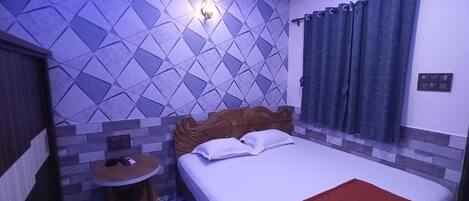 A bedroom with a bed, a small round table, a wall-mounted light, and a patterned wall.