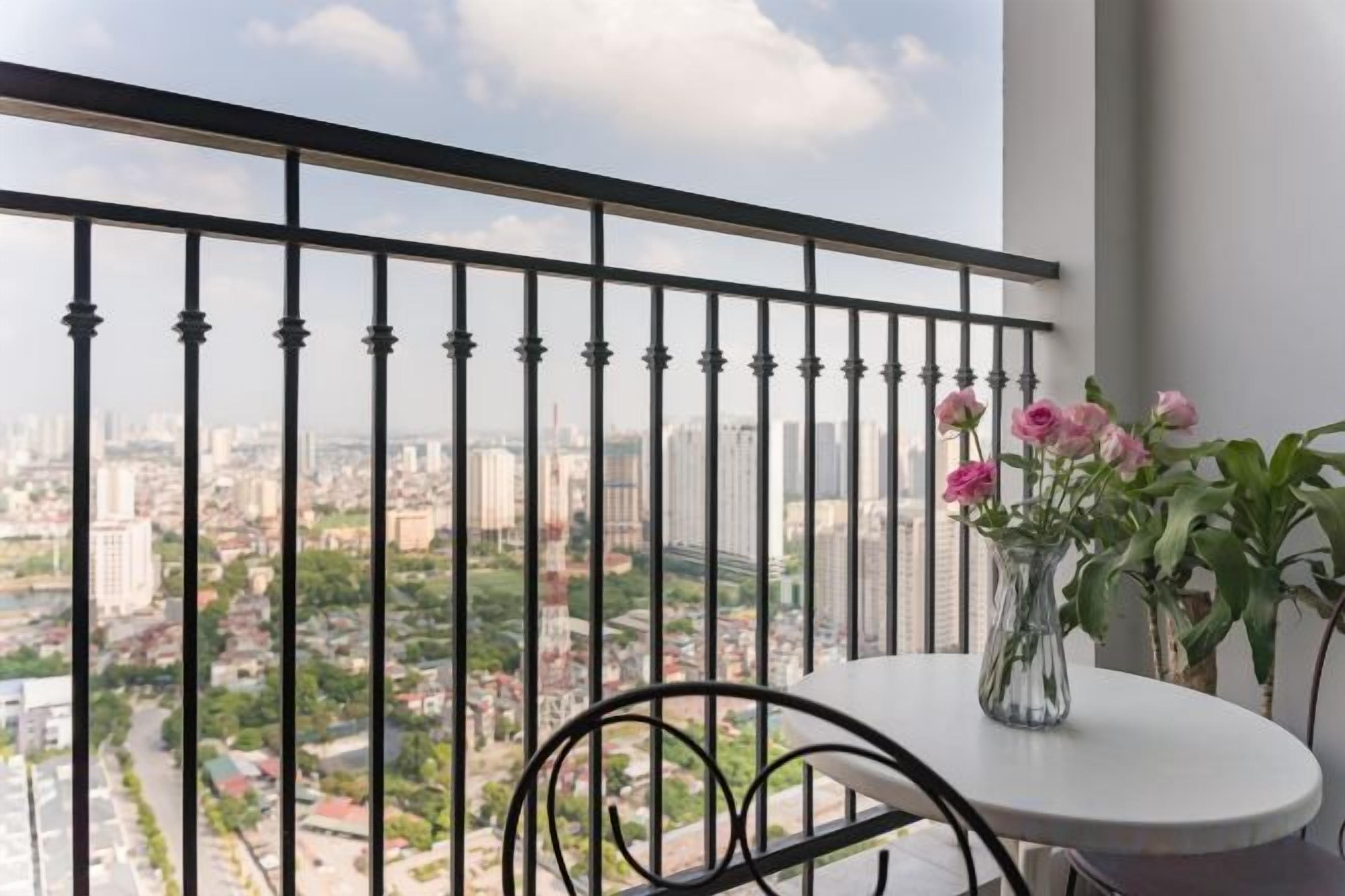 A balcony with a view of a cityscape, a table with a vase of flowers, and a chair.