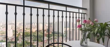 A balcony with a view of a cityscape, a table with a vase of flowers, and a chair.