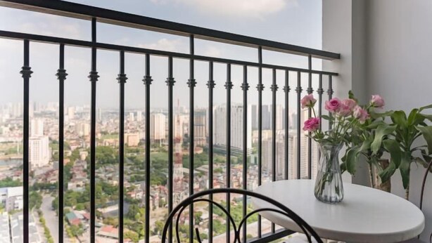 Een balkon met een metalen hekwerk, een ronde tafel met een bloevas, en een stadsgezicht op de achtergrond.