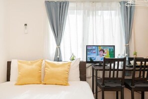 Une chambre d’hôtel avec un lit, deux oreillers jaunes, un bureau avec un ordinateur et une fenêtre avec des rideaux.