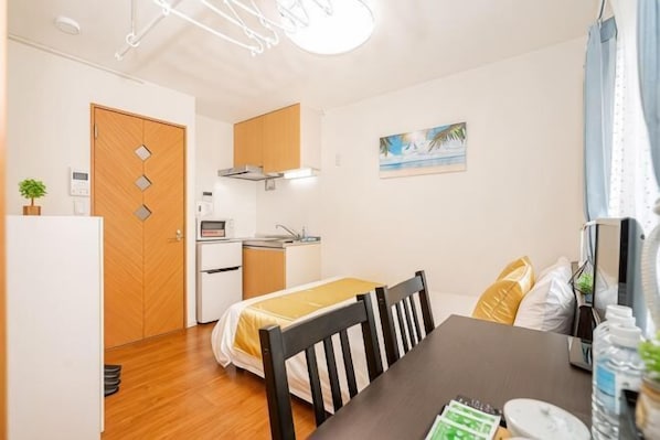 A compact room with a bed, a dining table, a kitchenette, and a door.