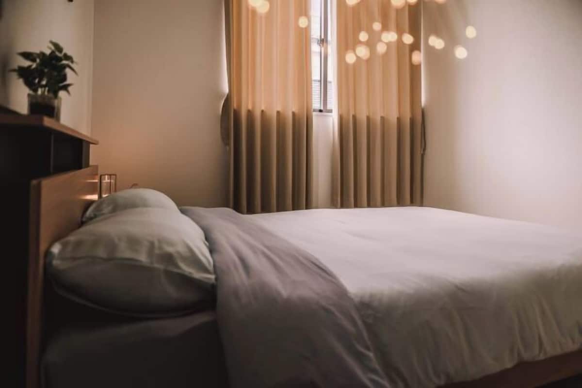 A neatly made bed with a white duvet and pillows, a bedside table with a lamp, and a window with curtains.