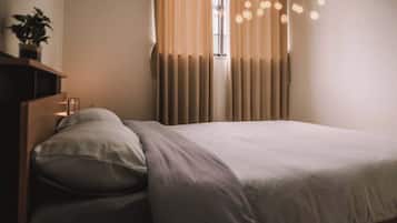 A neatly made bed with a white duvet and pillows, a bedside table with a lamp, and a window with curtains.